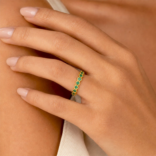 A close-up of a hand wearing a delicate gold eternity ring set with small round green gemstones.