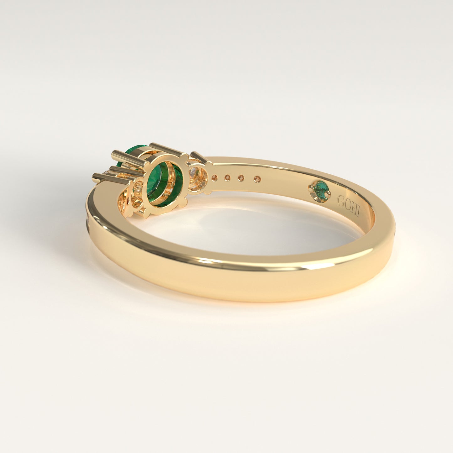 back view of a Trilogy Ring crafted in 18k yellow gold — a round green Colombian emerald at the center, flanked by two round diamonds, with smaller diamonds set along both shoulders.