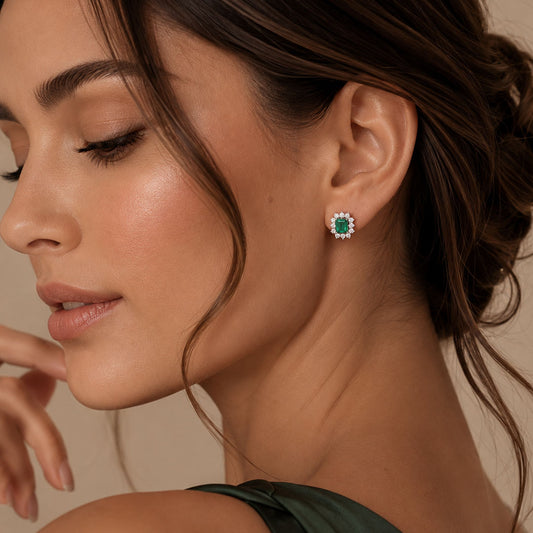 woman with white gold stud earrings featuring rectangular emerald-cut colombian emerald surrounded by small diamonds, photographed on a clean white background.
