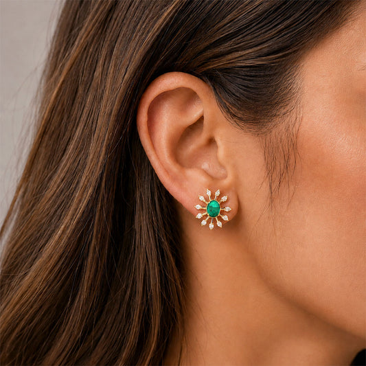 A close-up of a woman's ear wearing a small gold flower-shaped stud earring with a green center and diamondspetals.