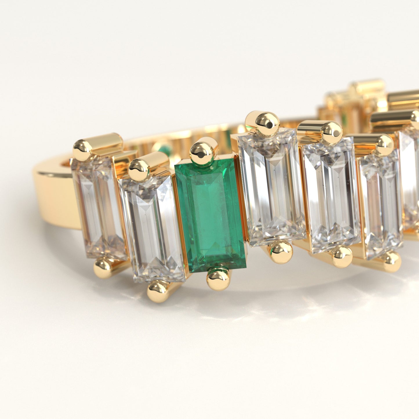 Zoom in of a yellow gold ring featuring a row of baguette-cut ciamonds and one baguette-cut colombian emerald, with a small round green gemstone on the inner band, set against a plain white background.