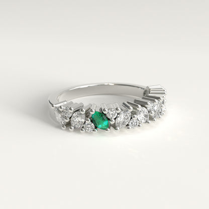 lateral view of a 18k white gold diamond band ring featuring a row of marquise-cut and round diamonds with a single prominent green marquise emerald on the left, set against a clean white background.