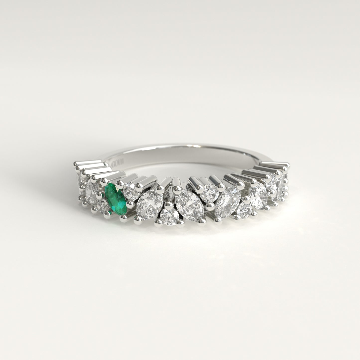 A 18k white gold diamond band ring featuring a row of marquise-cut and round diamonds with a single prominent green marquise emerald on the left, set against a clean white background.