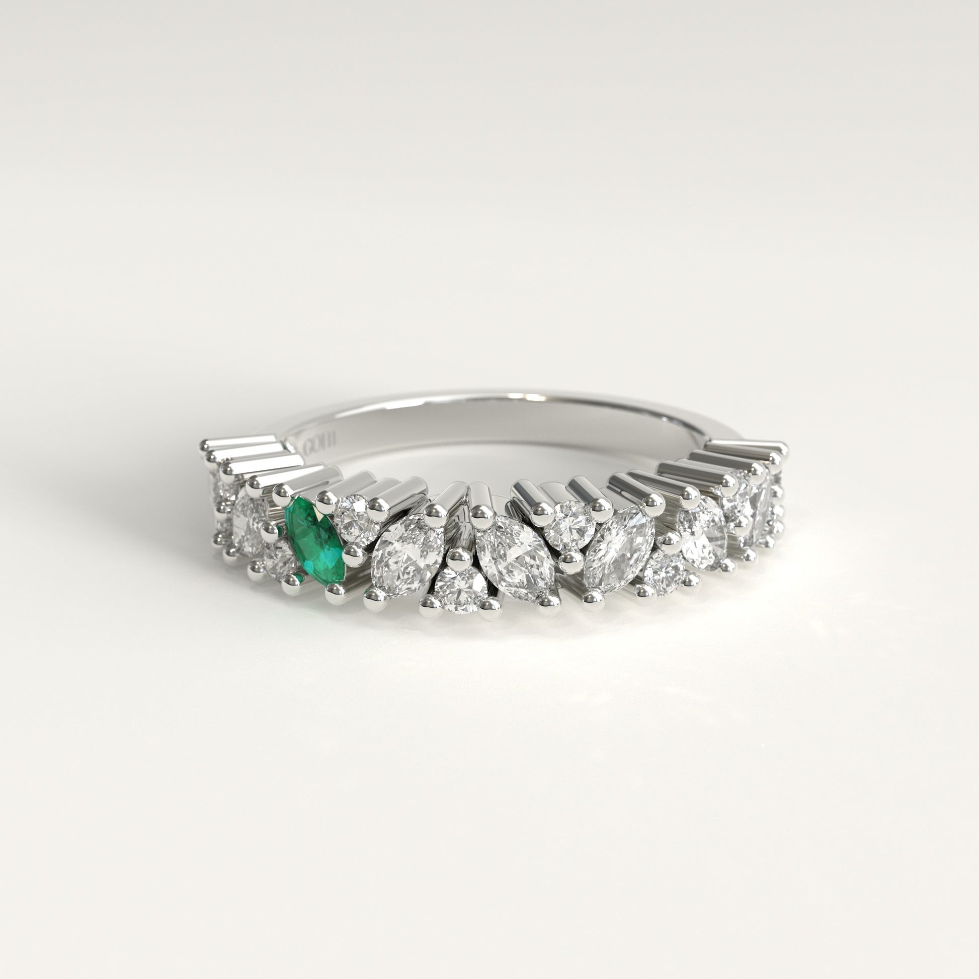 A 18k white gold diamond band ring featuring a row of marquise-cut and round diamonds with a single prominent green marquise emerald on the left, set against a clean white background.