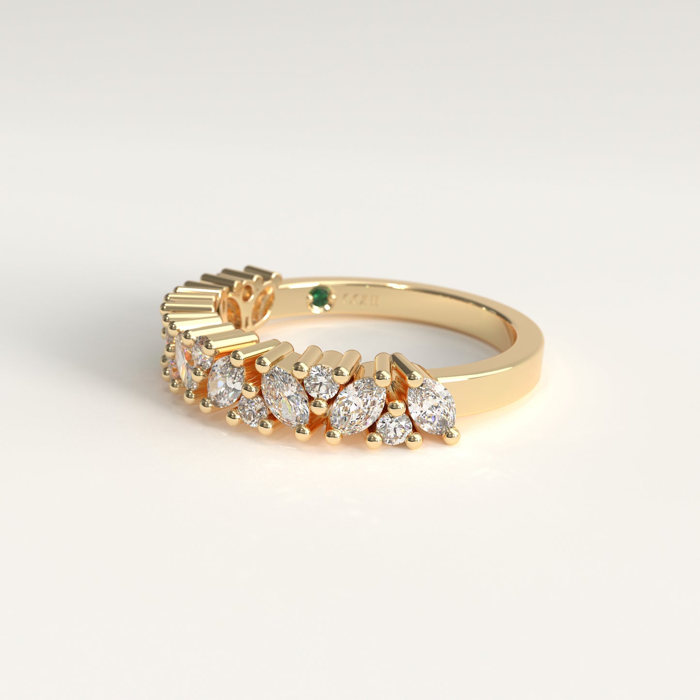 A yellow gold ring featuring a row of marquise-cut and round diamonds, with a small green emerald on the band, shown on a clean white background.