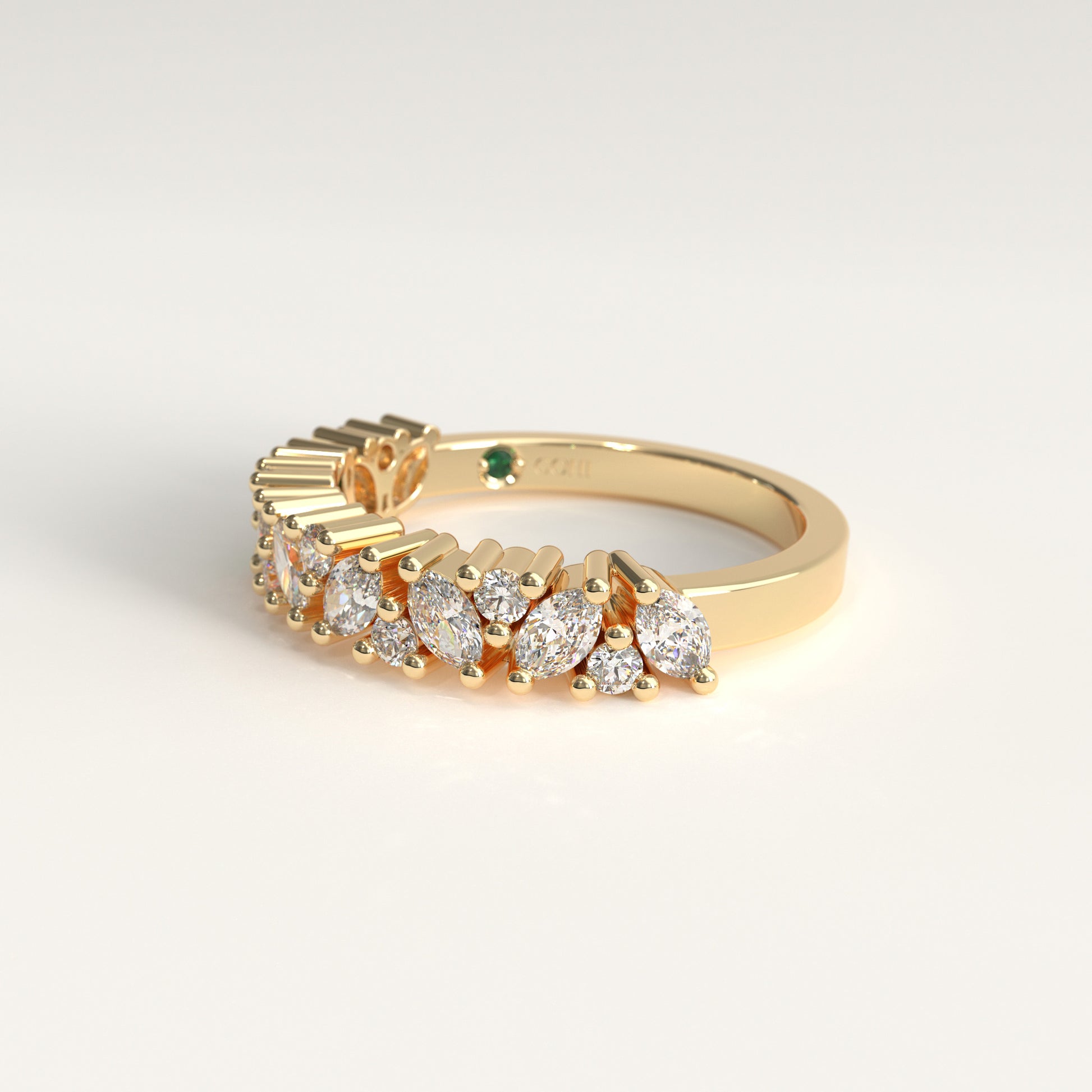 A yellow gold ring featuring a row of marquise-cut and round diamonds, with a small green emerald on the band, shown on a clean white background.