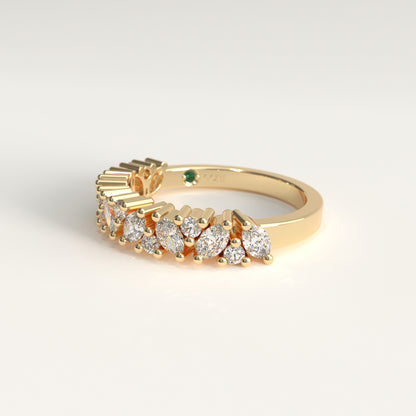A yellow gold ring featuring a row of marquise-cut and round diamonds, with a small green emerald on the band, shown on a clean white background.