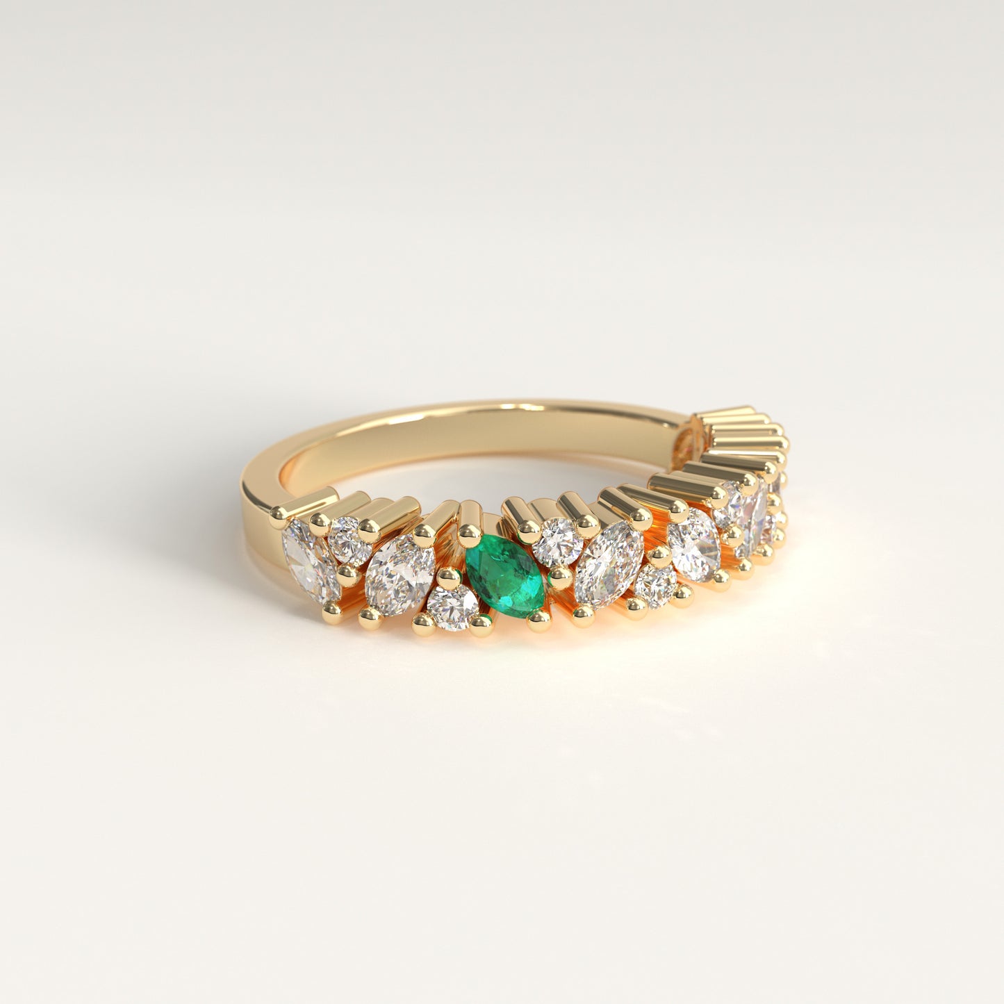 lateral view of a yellow gold eternity-style ring featuring a row of round and marquise-cut diamonds with a central green marquise cut emerald, photographed on a clean light gray background.