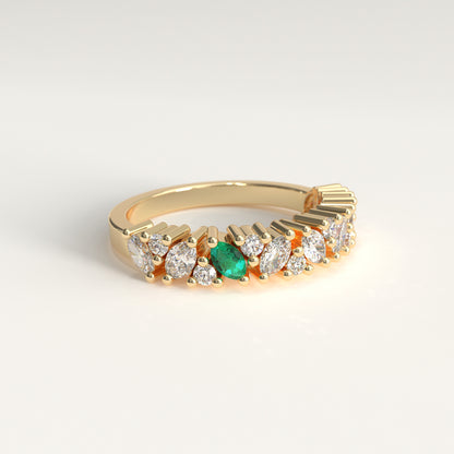 lateral view of a yellow gold eternity-style ring featuring a row of round and marquise-cut diamonds with a central green marquise cut emerald, photographed on a clean light gray background.