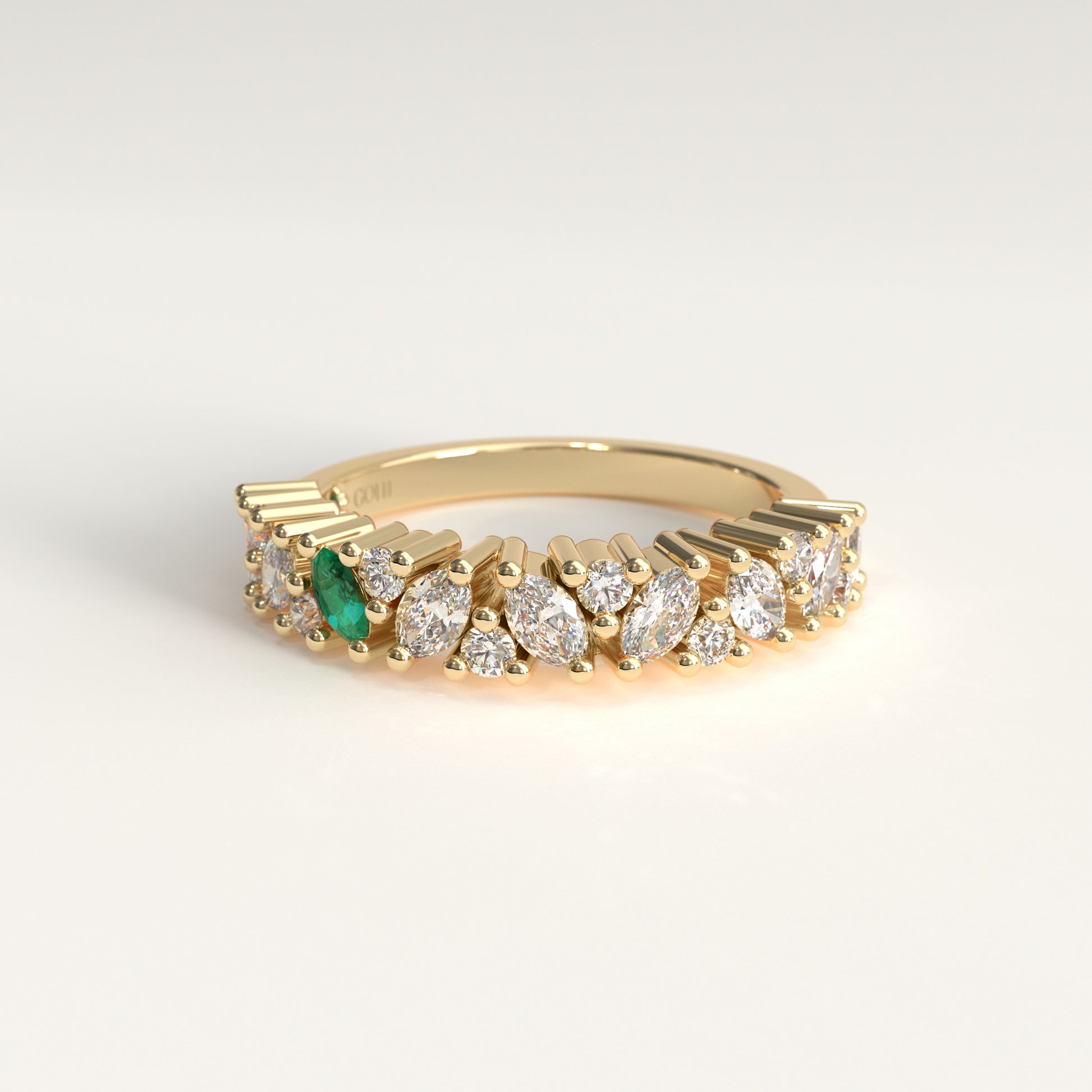 A yellow 18 k gold eternity-style ring featuring a row of round and marquise-cut diamonds with one prominent colombian emerald marquise-cut, shown on a light gray background.