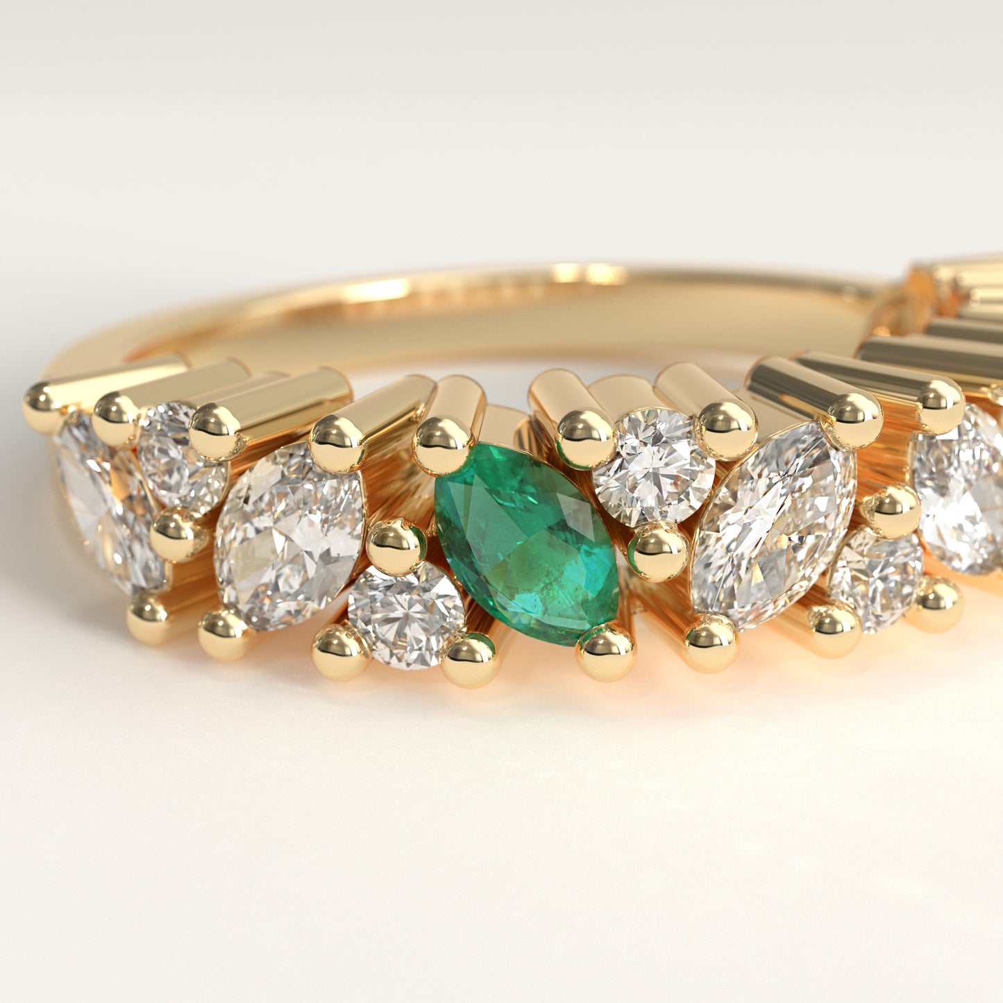 close up of a yellow gold eternity-style ring featuring a row of round and marquise-cut diamonds with a central green marquise cut emerald, photographed on a clean light gray background.