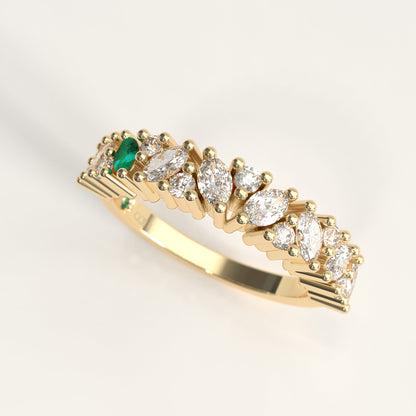 A 18k yellow gold eternity-style ring featuring a row of round and marquise-cut diamonds with a central green marquise cut emerald, photographed on a clean light gray background.