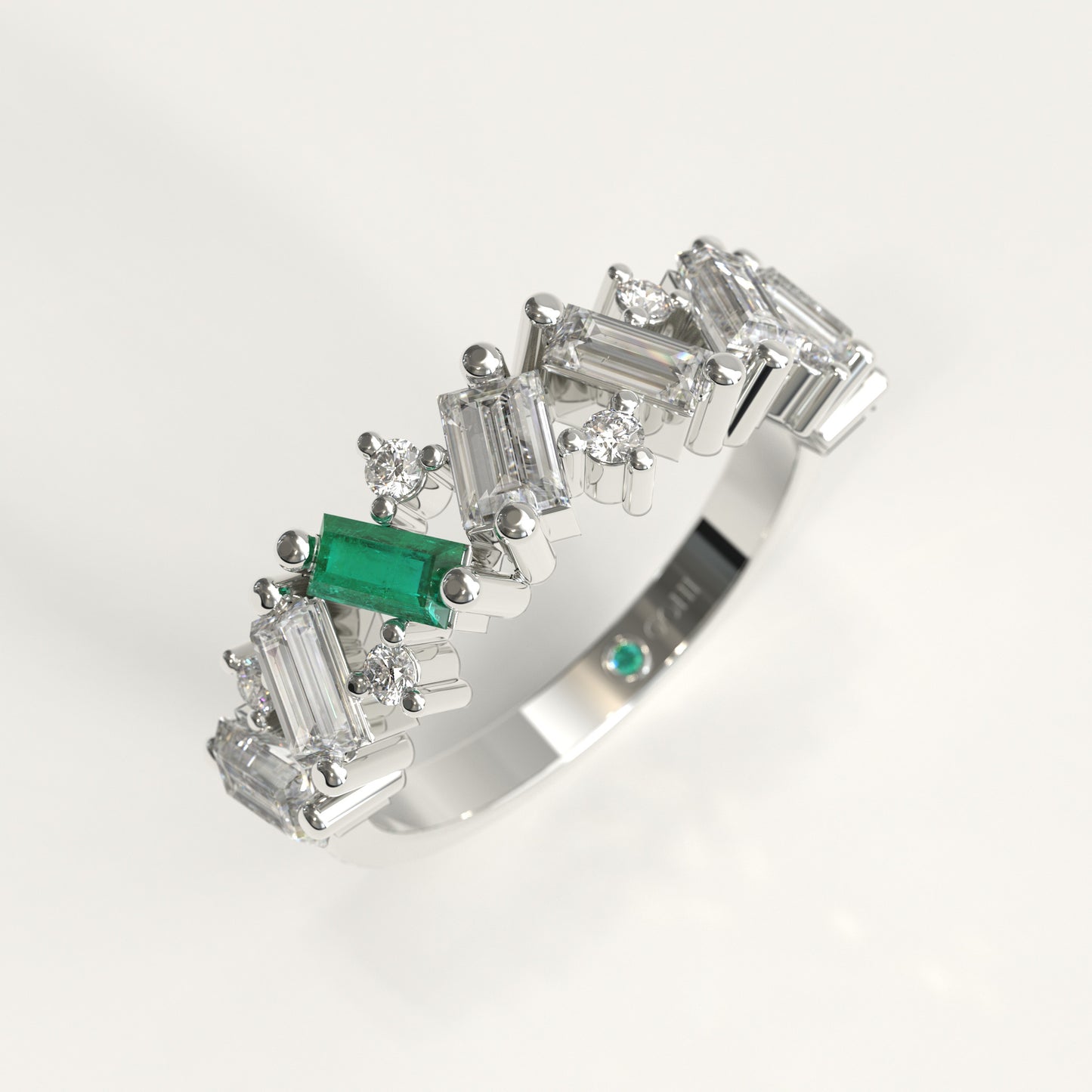 A White 18k gold band ring featuring a row of baguette and round Diamonds, accented by a prominent Colombian emerald emerald-cut center stone and a small matching green stone on the inner band, shown on a white background.