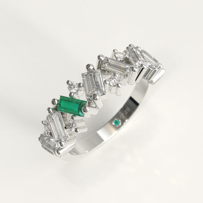 A White 18k gold band ring featuring a row of baguette and round Diamonds, accented by a prominent Colombian emerald emerald-cut center stone and a small matching green stone on the inner band, shown on a white background.