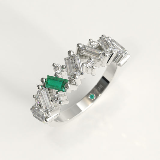A White 18k gold band ring featuring a row of baguette and round Diamonds, accented by a prominent Colombian emerald emerald-cut center stone and a small matching green stone on the inner band, shown on a white background.