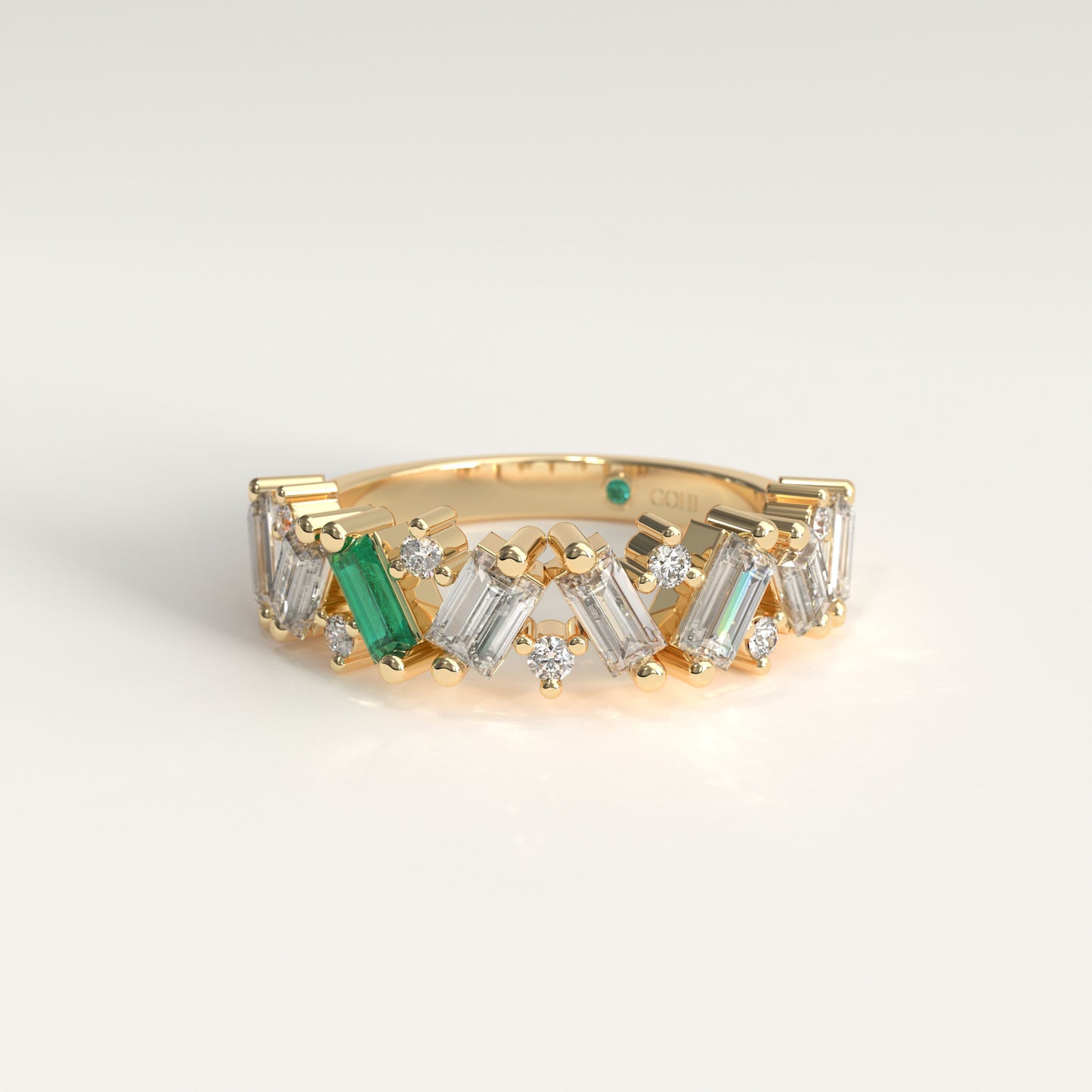 A yellow gold ring featuring a row of baguette and round natural diamons, accented by a Colombian Emerald, shown on a light gray background.