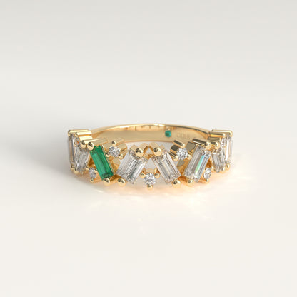 A yellow gold ring featuring a row of baguette and round natural diamons, accented by a Colombian Emerald, shown on a light gray background.