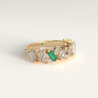 A 18k fairmined gold band ring featuring a row of diamonds baguette and round-cut  with a prominent green Colombian emerald emerald-cut center stone, photographed on a clean white background.