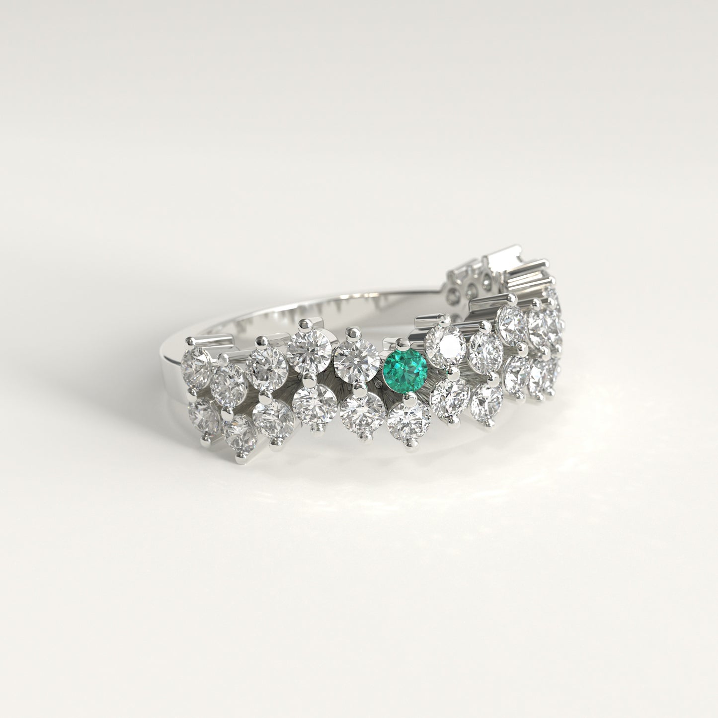 Lateral view of a Stratum Ring in 18k fairmined white gold with a tiered row of round brilliant diamonds set in a zigzag pattern, and one round Colombian emerald bezel-set among them at the center. Smooth polished white gold band beneath the sparkling stone clusterer