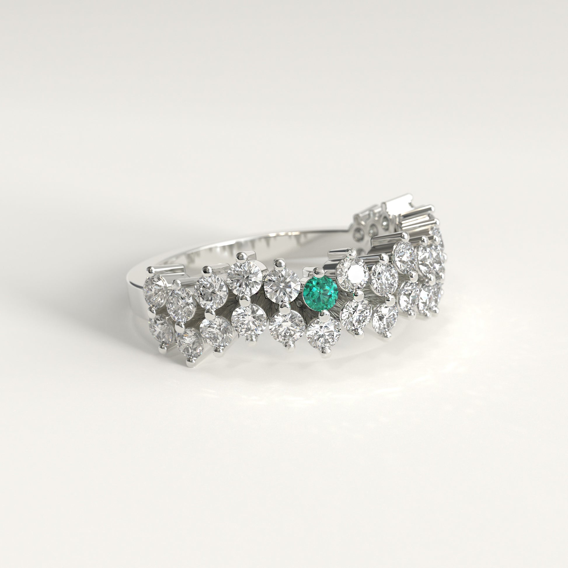 Lateral view of a Stratum Ring in 18k fairmined white gold with a tiered row of round brilliant diamonds set in a zigzag pattern, and one round Colombian emerald bezel-set among them at the center. Smooth polished white gold band beneath the sparkling stone clusterer