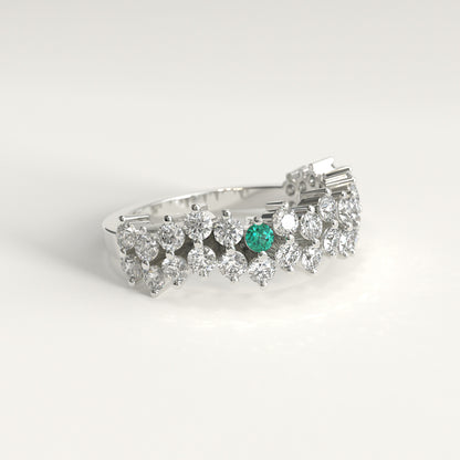Lateral view of a Stratum Ring in 18k fairmined white gold with a tiered row of round brilliant diamonds set in a zigzag pattern, and one round Colombian emerald bezel-set among them at the center. Smooth polished white gold band beneath the sparkling stone clusterer