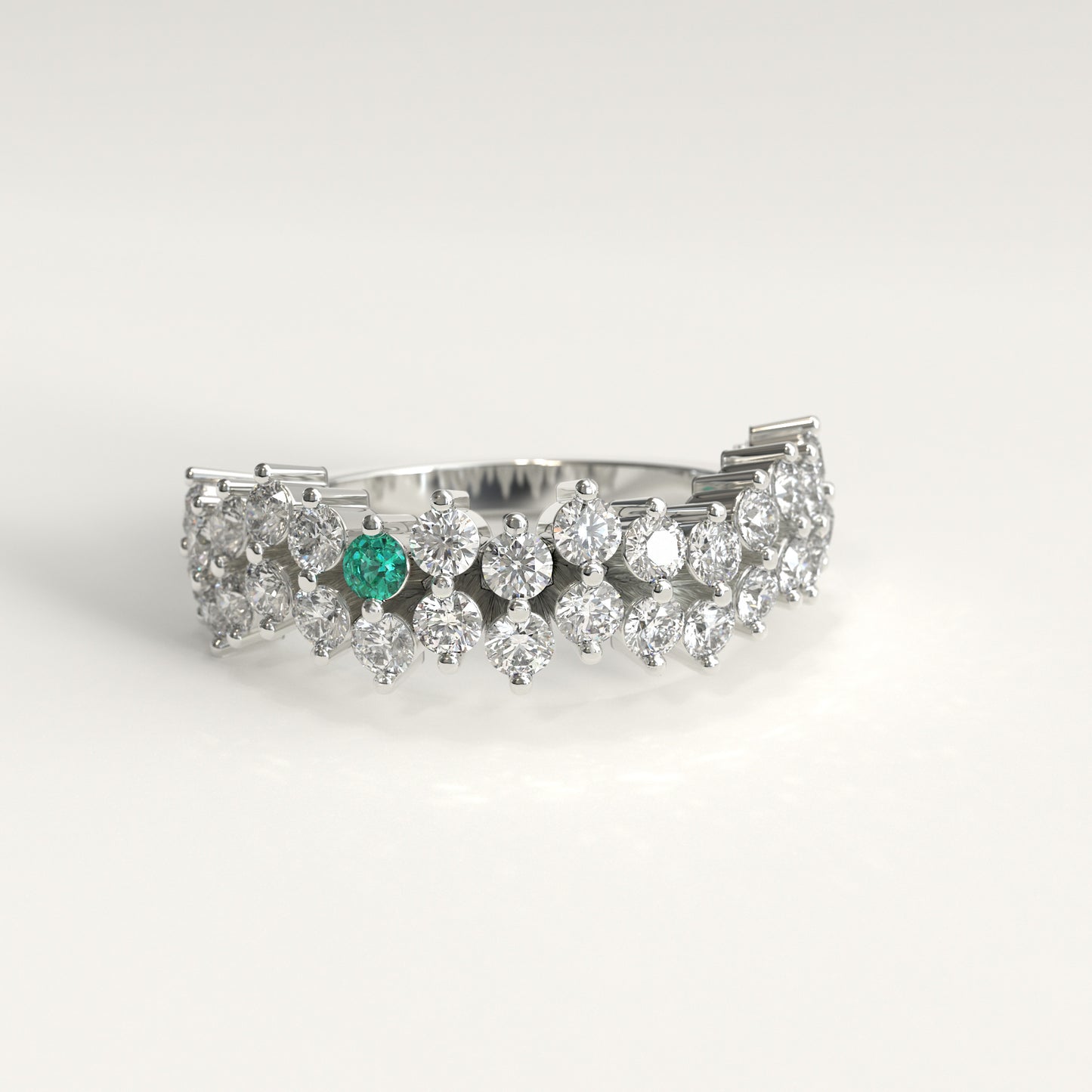 Stratum Ring in 18k fairmined white gold with a tiered row of round brilliant diamonds set in a zigzag pattern, and one round Colombian emerald bezel-set among them at the center. Smooth polished white gold band beneath the sparkling stone cluster
