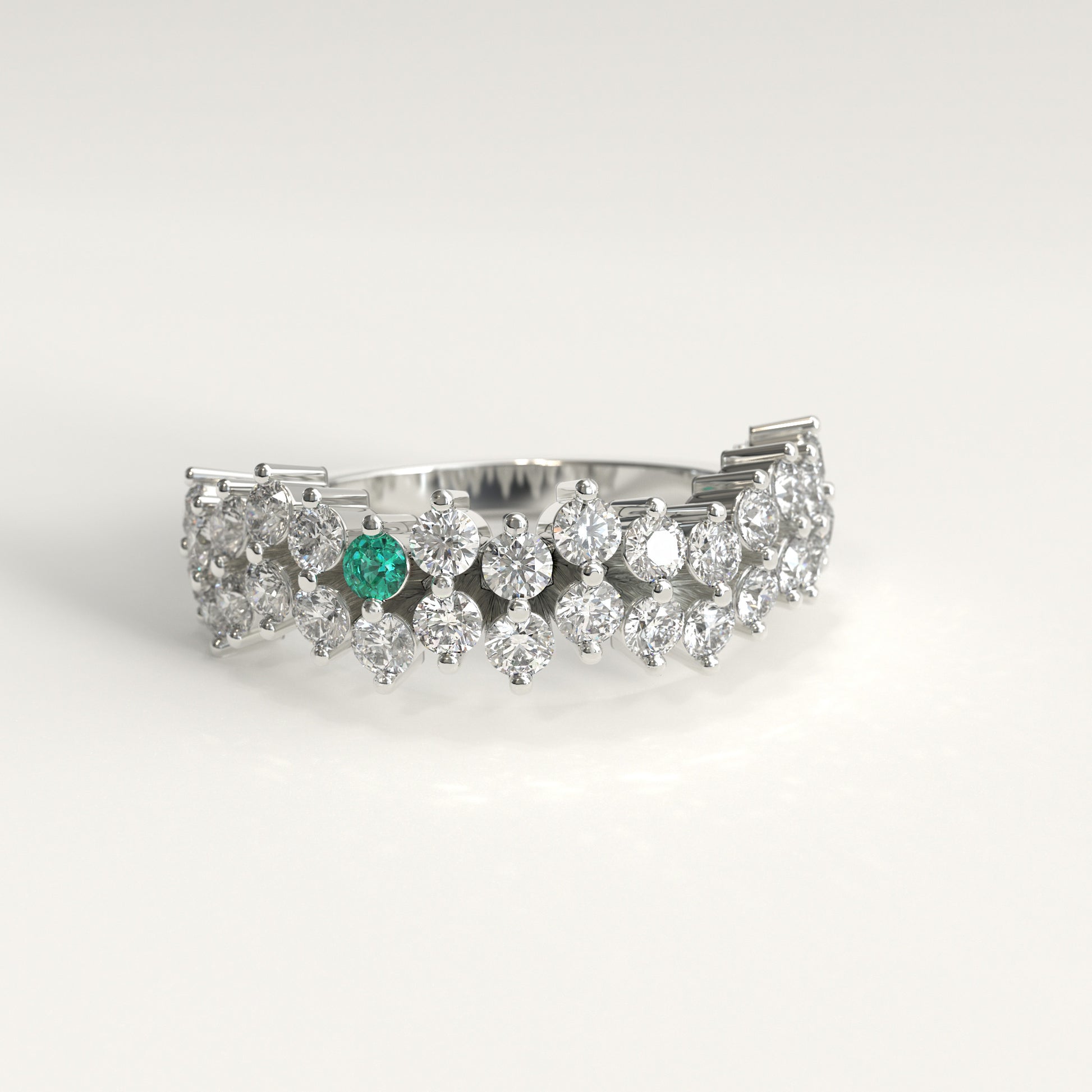 Stratum Ring in 18k fairmined white gold with a tiered row of round brilliant diamonds set in a zigzag pattern, and one round Colombian emerald bezel-set among them at the center. Smooth polished white gold band beneath the sparkling stone cluster