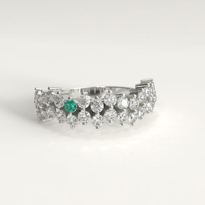 Stratum Ring in 18k fairmined white gold with a tiered row of round brilliant diamonds set in a zigzag pattern, and one round Colombian emerald bezel-set among them at the center. Smooth polished white gold band beneath the sparkling stone cluster