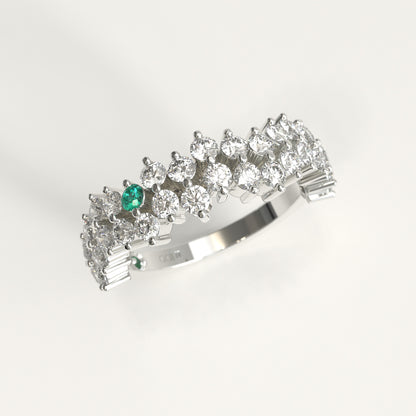 Stratum Ring in 18k fairmined white gold with a tiered row of round brilliant diamonds set in a zigzag pattern, and one round Colombian emerald bezel-set among them at the center. Smooth polished white gold band beneath the sparkling stone cluster