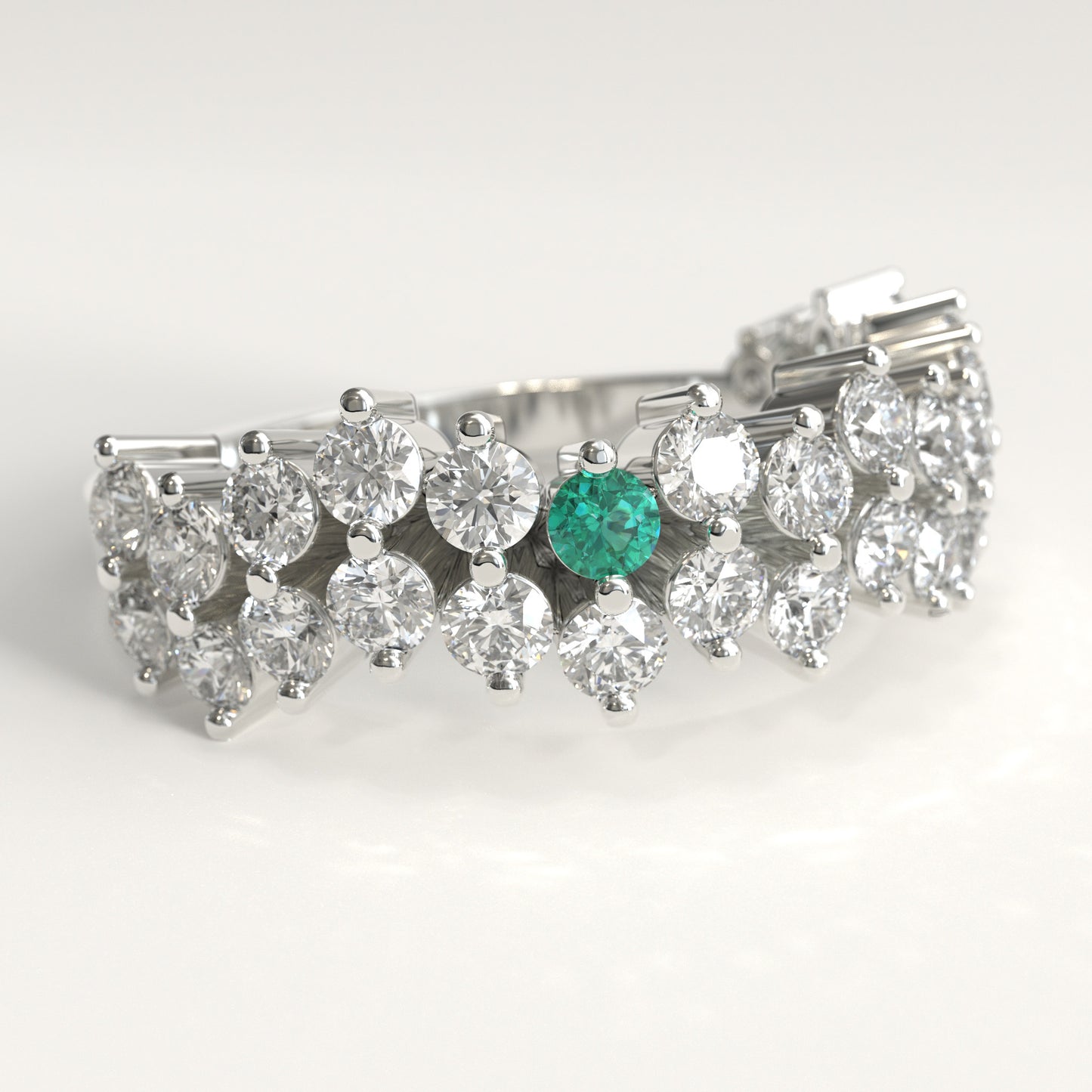 datail view of a Stratum Ring in 18k fairmined white gold with a tiered row of round brilliant diamonds set in a zigzag pattern, and one round Colombian emerald bezel-set among them at the center. Smooth polished white gold band beneath the sparkling stone cluster