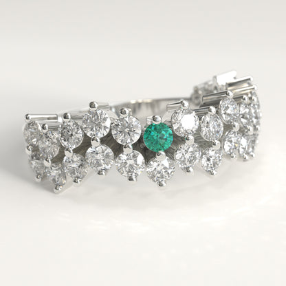datail view of a Stratum Ring in 18k fairmined white gold with a tiered row of round brilliant diamonds set in a zigzag pattern, and one round Colombian emerald bezel-set among them at the center. Smooth polished white gold band beneath the sparkling stone cluster
