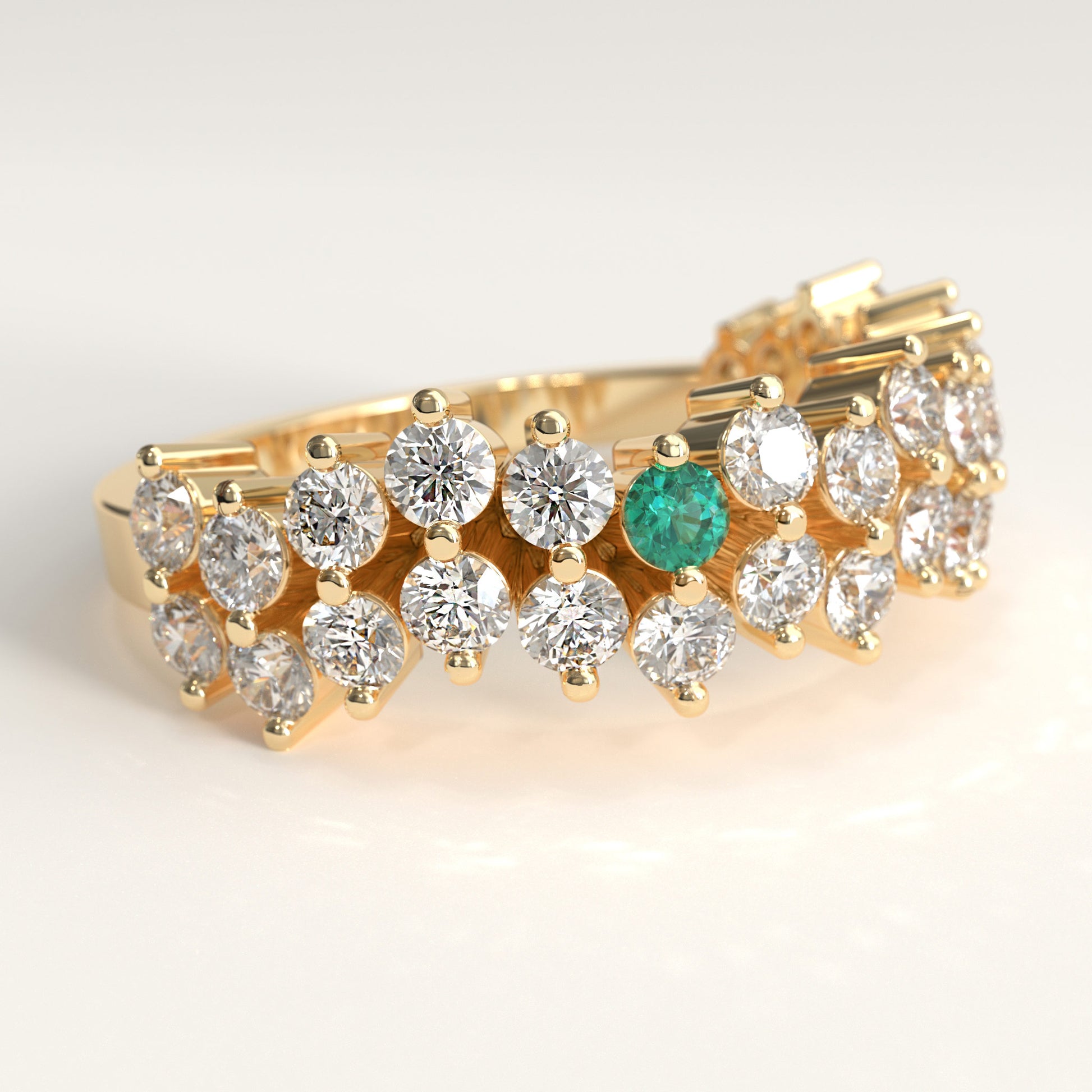 detail view of a Stratum Ring in 18k fairmined yellow gold with a tiered row of round brilliant diamonds set in a zigzag pattern, and one round Colombian emerald bezel-set among them at the center. Smooth polished white gold band beneath the sparkling stone cluster