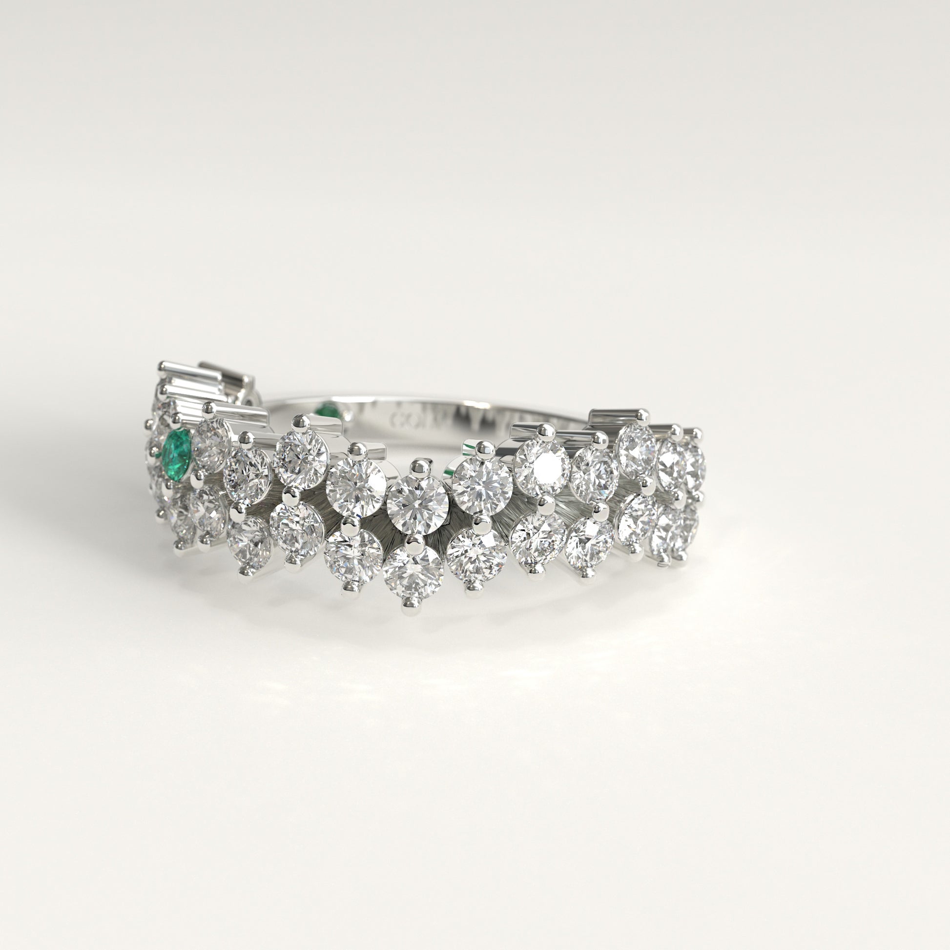lateral view of Stratum Ring in 18k fairmined white gold with a tiered row of round brilliant diamonds set in a zigzag pattern, and one round Colombian emerald bezel-set among them at the center. Smooth polished white gold band beneath the sparkling stone cluster