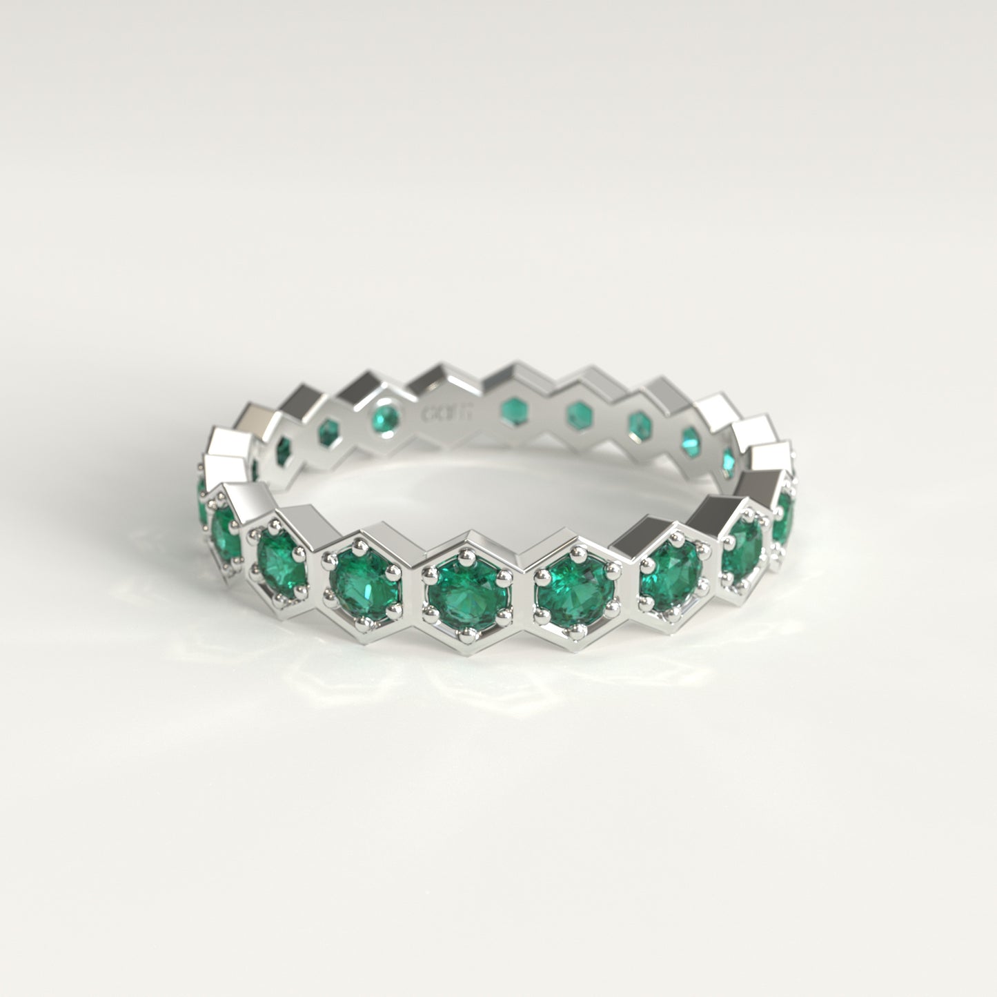 A white gold eternity ring featuring a repeating hexagonal pattern with round cut colombian emerald, set against a clean white background.
