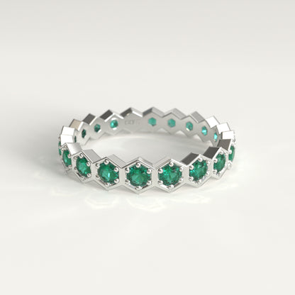 A white gold eternity ring featuring a repeating hexagonal pattern with round cut colombian emerald, set against a clean white background.