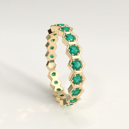 A 18 fairmined yellow gold hexagonal eternity ring featuring round-cut colombian emeralds, displayed on a clean white background.