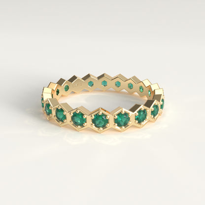 A gold eternity ring featuring a repeating hexagonal pattern with round-cut green emerald gemstones, shown on a clean white background.