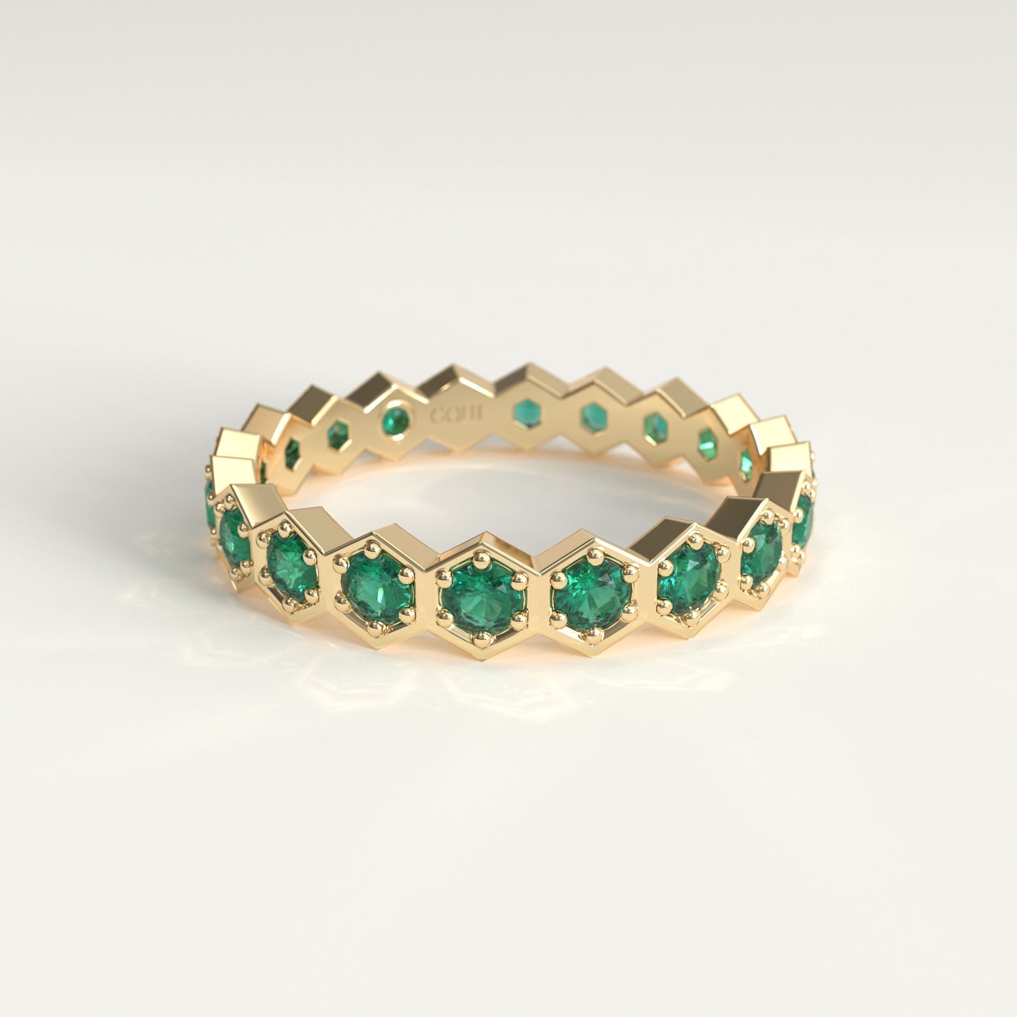 A gold eternity ring featuring a continuous hexagon pattern of round-cut green emerald gemstones, set against a clean white background.