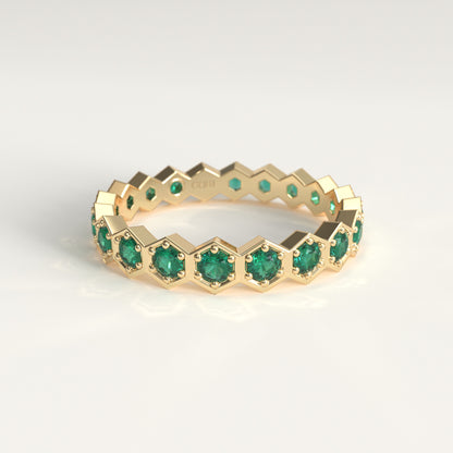 A gold eternity ring featuring a continuous hexagon pattern of round-cut green emerald gemstones, set against a clean white background.