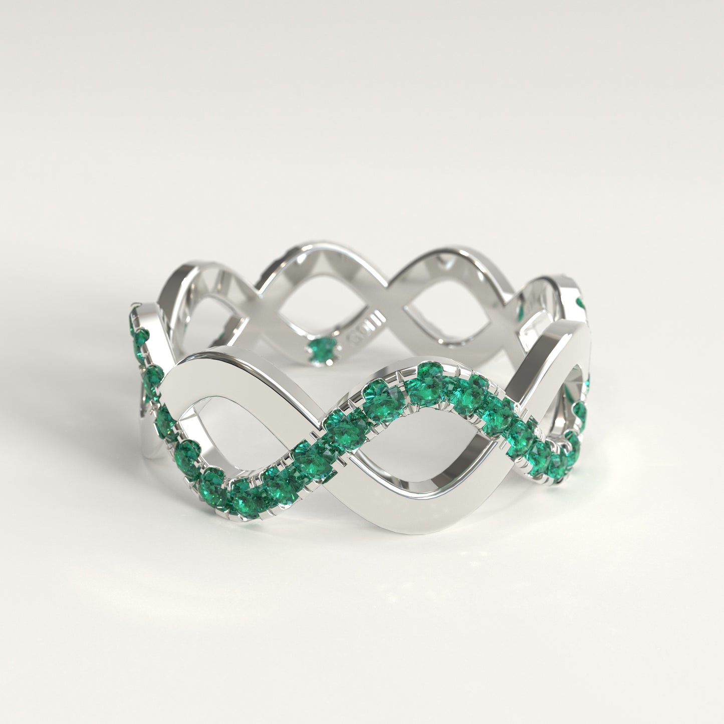 A 18k fairmined white gold infinity-style ring adorned with a row of colombian emeralds, photographed on a clean white background.