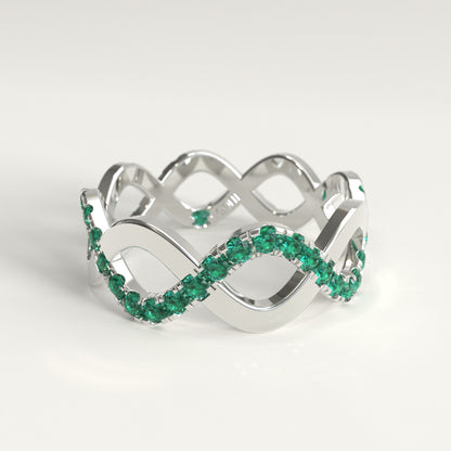 A 18k fairmined white gold infinity-style ring adorned with a row of colombian emeralds, photographed on a clean white background.