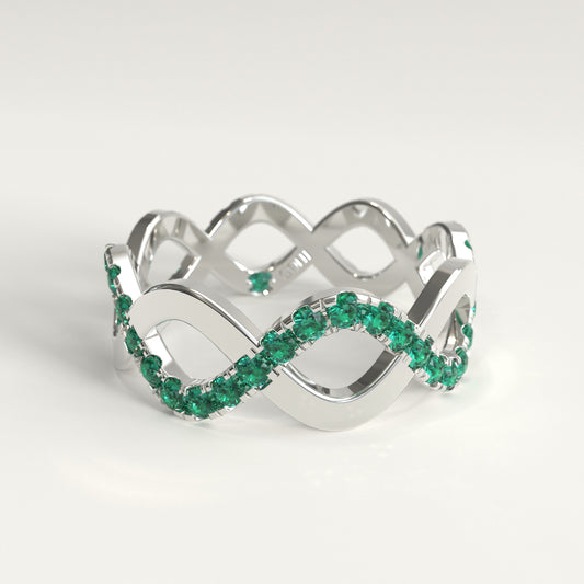 A 18k fairmined white gold infinity-style ring adorned with a row of colombian emeralds, photographed on a clean white background.