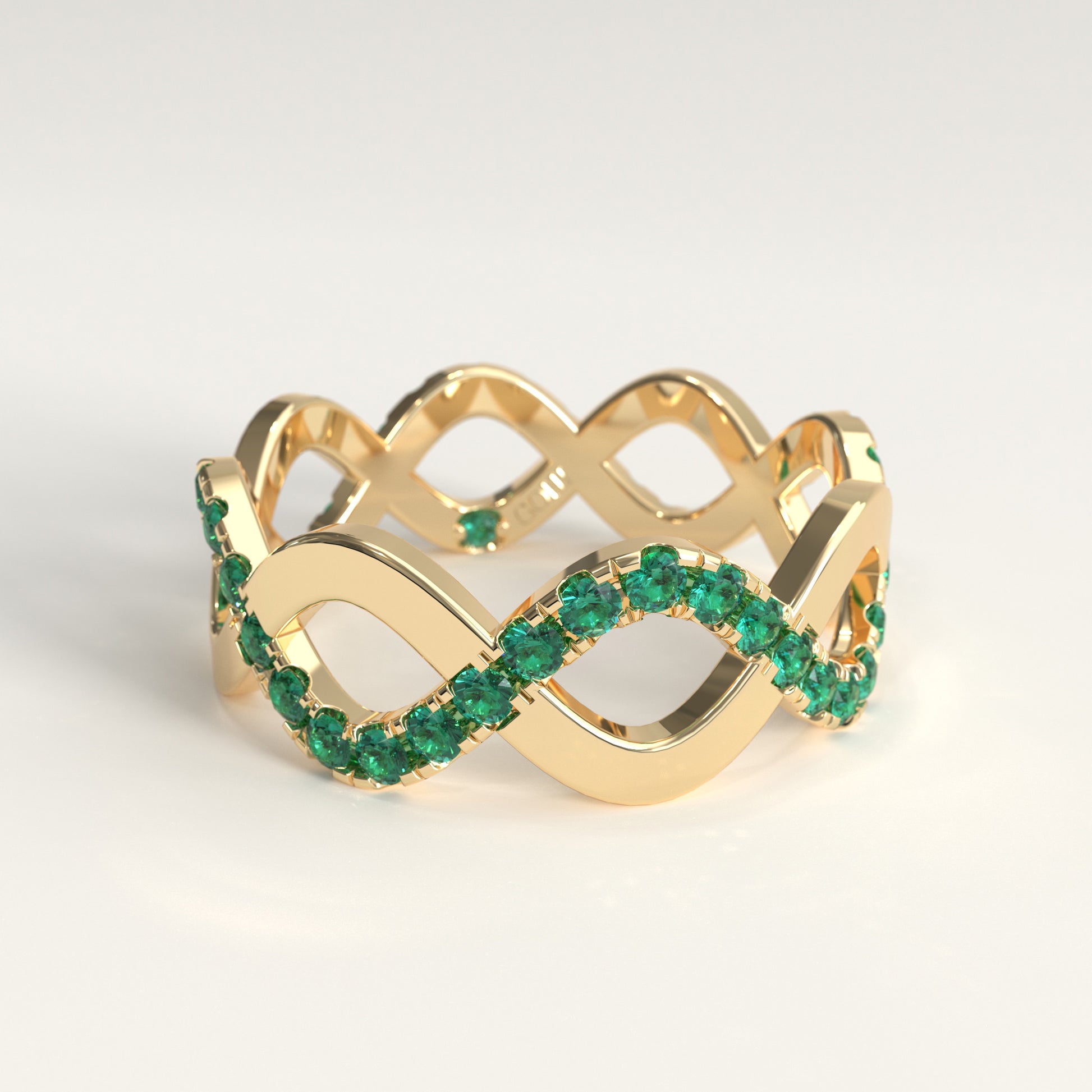 A 18k fairmined yellow gold infinity-style ring adorned with round colombian emeralds along the lower curve, photographed on a clean light gray background.