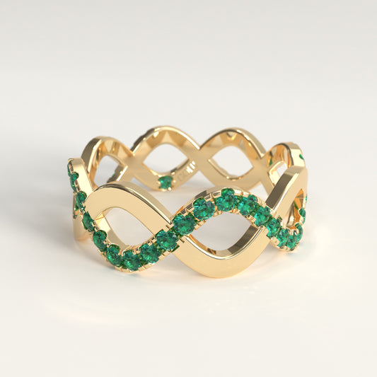 A 18k fairmined yellow gold infinity-style ring adorned with round colombian emeralds along the lower curve, photographed on a clean light gray background.