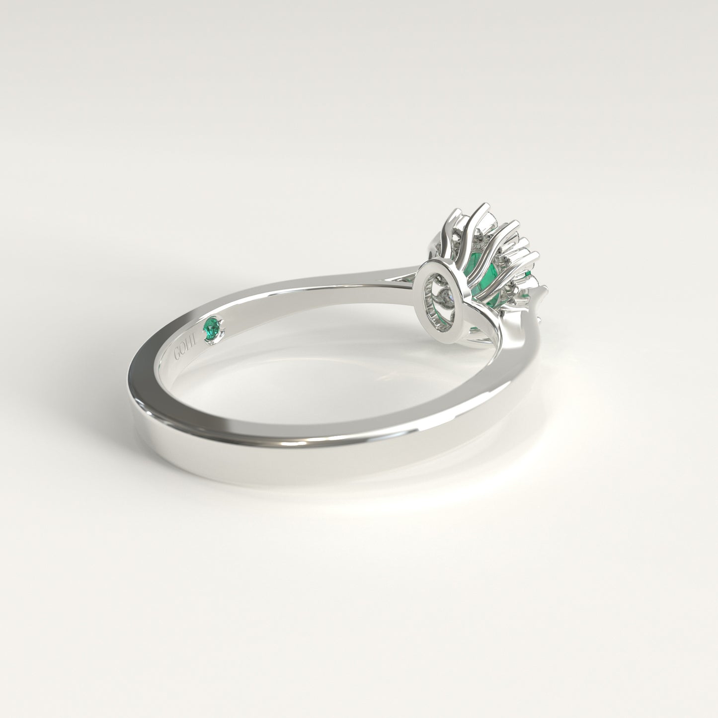 Back view of the ring's underside, showing the gold prongs cradling the emerald from below and, just beside the GOHI signature engraved inside the band, a tiny hidden emerald catching a glint of green.