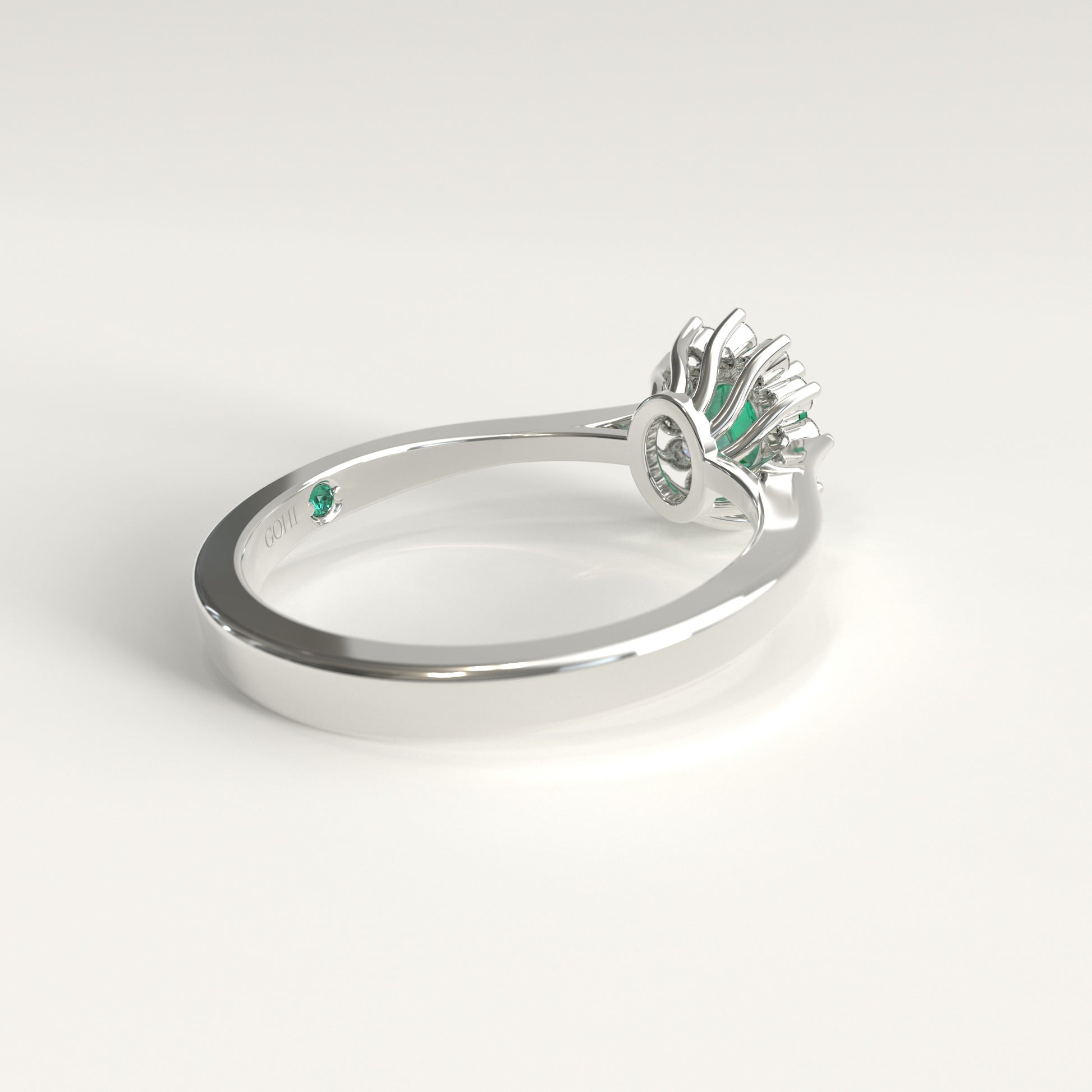 Back view of the ring's underside, showing the gold prongs cradling the emerald from below and, just beside the GOHI signature engraved inside the band, a tiny hidden emerald catching a glint of green.