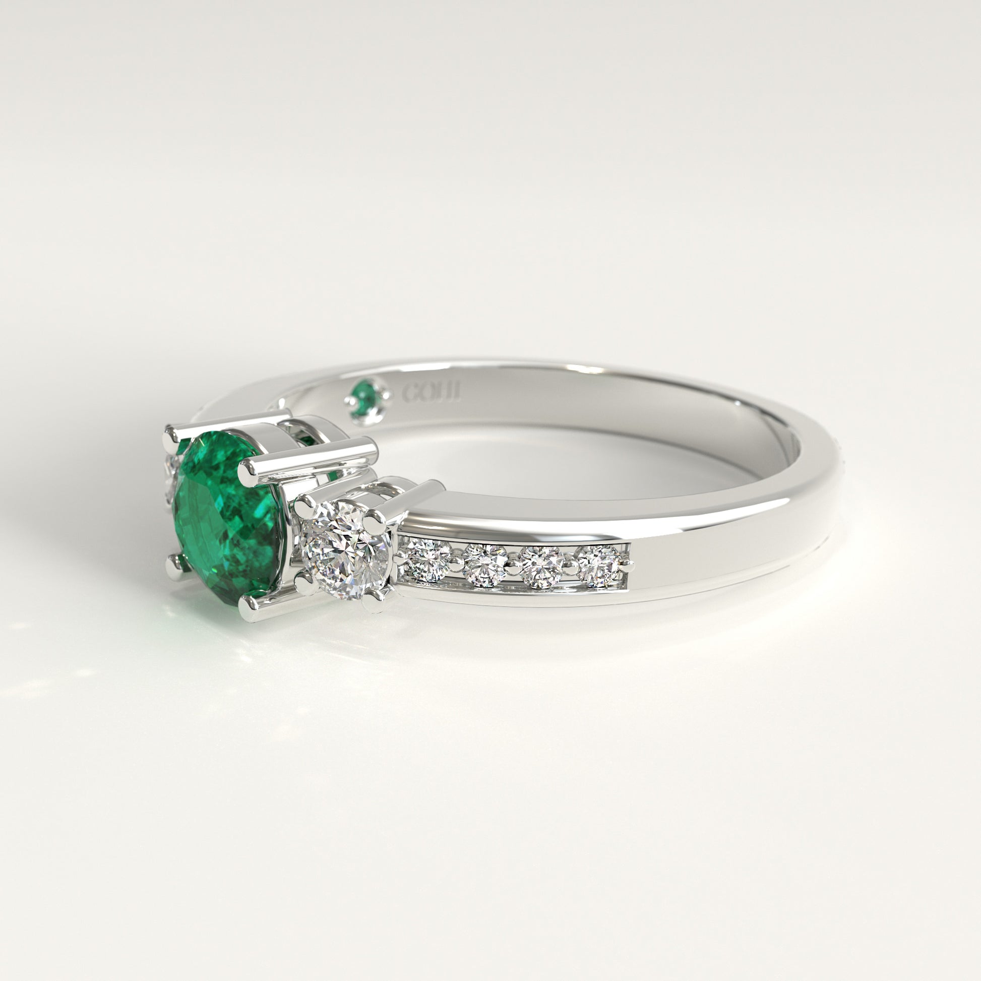 Lateral view of the ring's underside, showing the prong settings holding the emerald and diamonds from below, with the GOHI signature engraved inside the band beside a tiny hidden emerald.