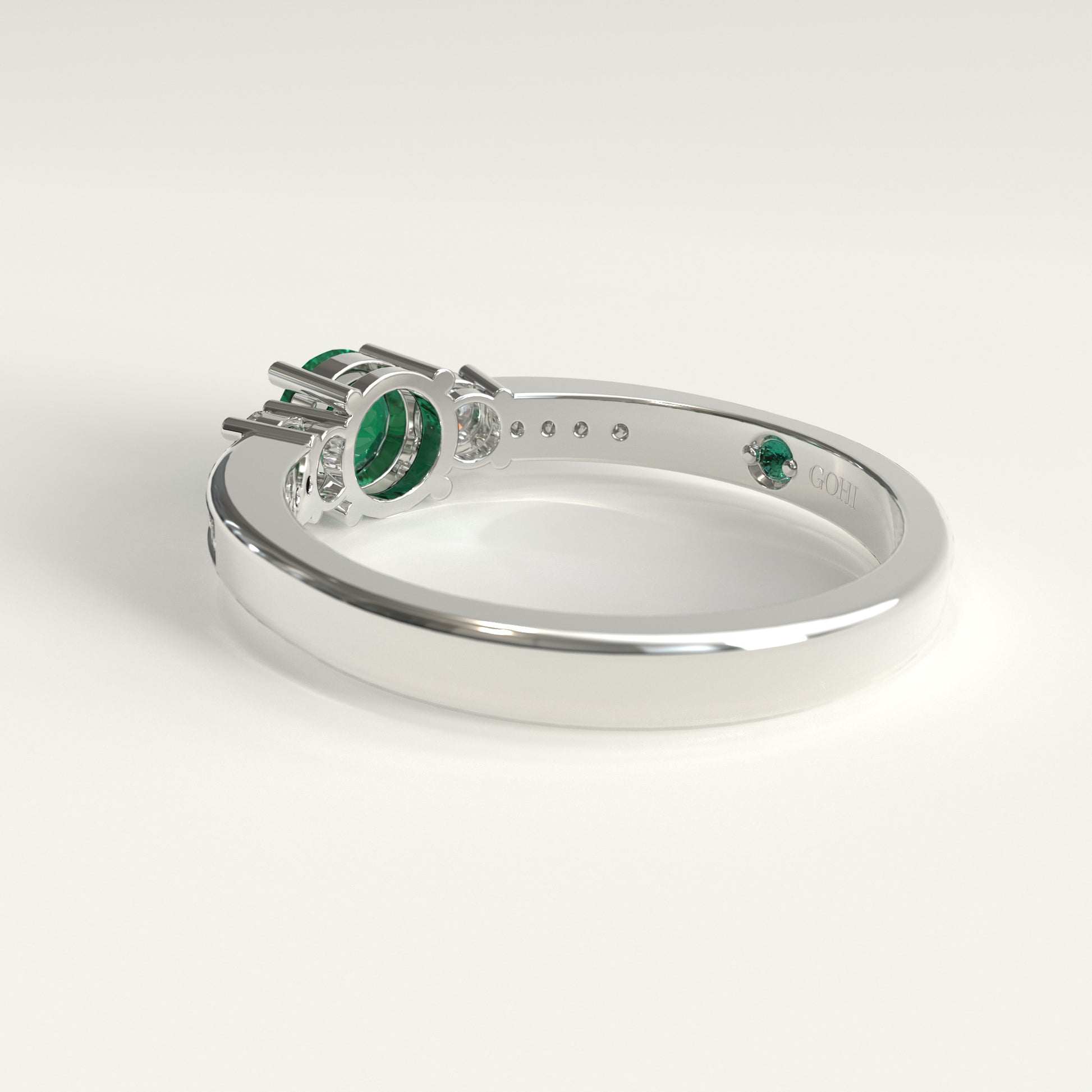 Back view of the ring's underside, showing the prong settings holding the emerald and diamonds from below, with the GOHI signature engraved inside the band beside a tiny hidden emerald.