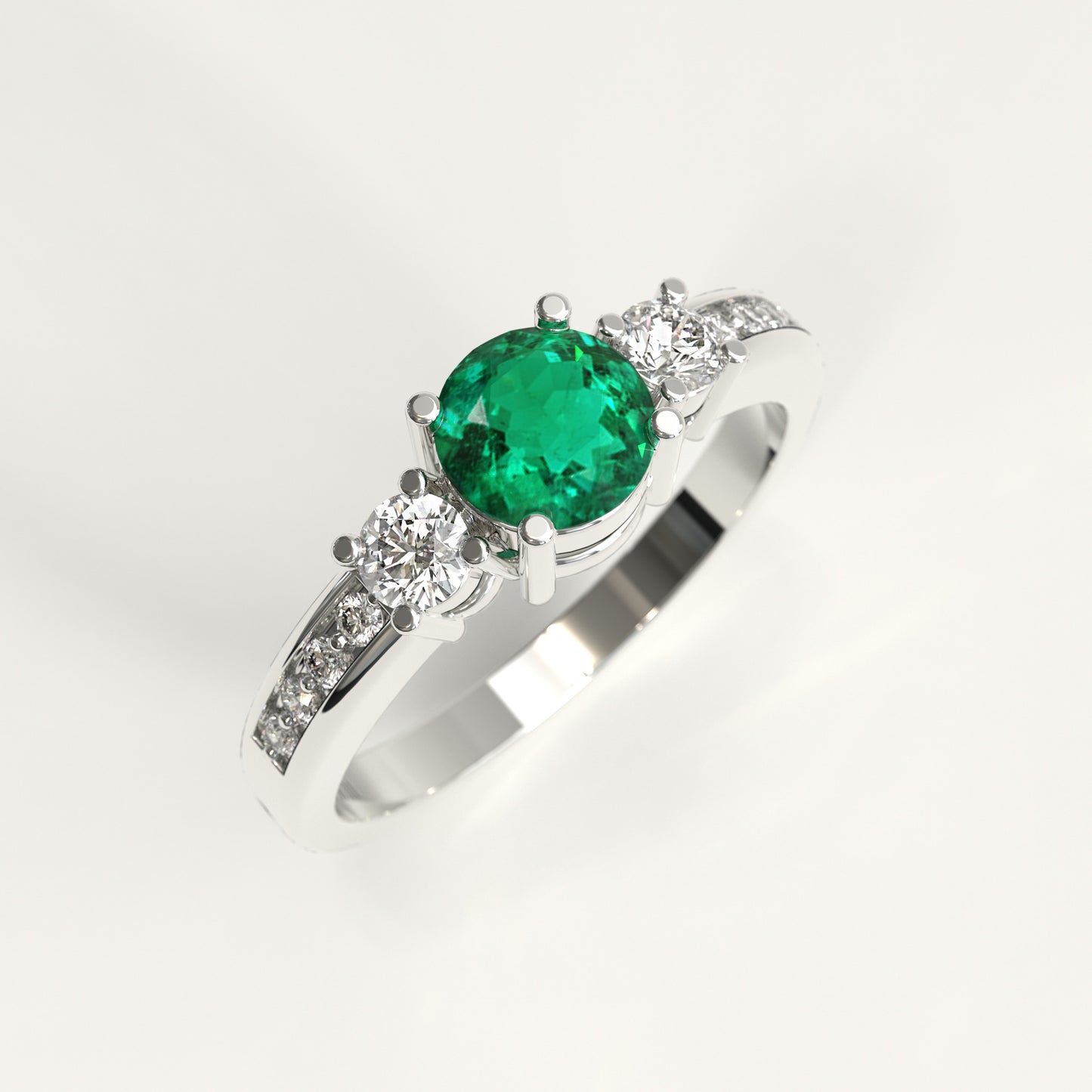 A 18k fairmined gold ring featuring a round-cut green colombian emerald center stone and small diamonds accent stones on the shoulders, set against a plain white background.