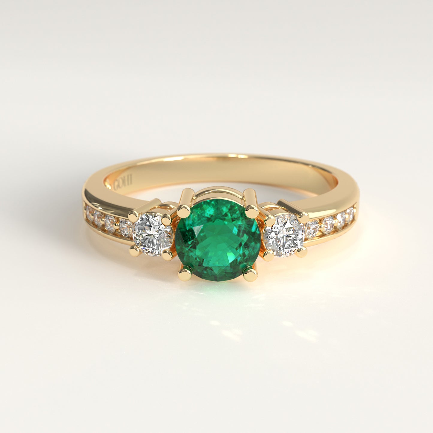 The same Trilogy Ring crafted in 18k yellow gold — a round green Colombian emerald at the center, flanked by two round diamonds, with smaller diamonds set along both shoulders.